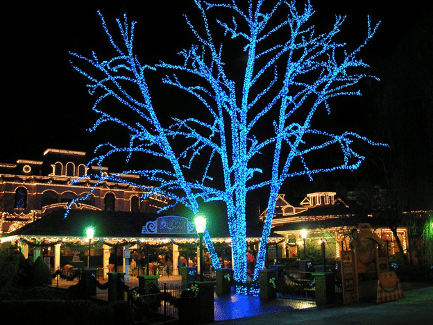 Festive winter lights display at Dollywood in Pigeon Forge, featuring a blue-lit tree & buildings outlined in warm lights.