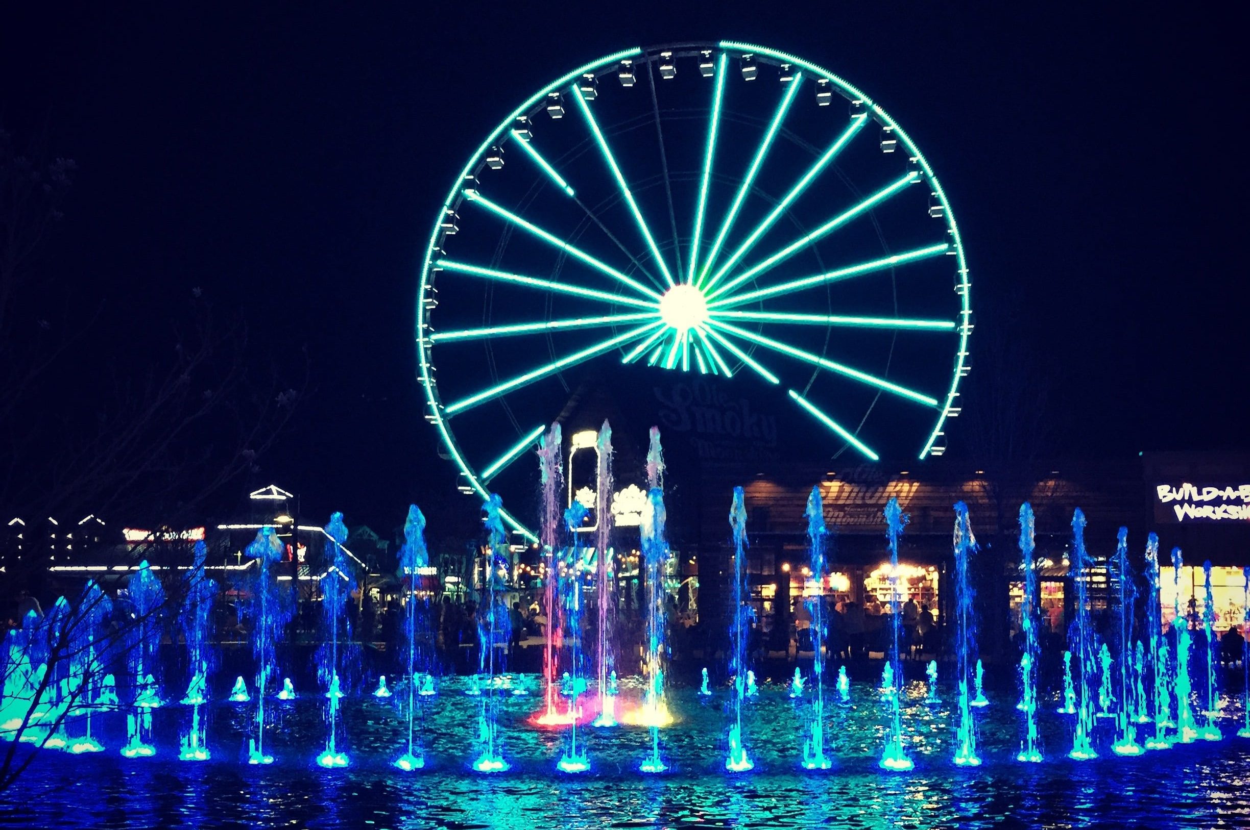 Illuminated Ferris wheel and dancing fountains at The Island in Pigeon Forge at night, with blue and turquoise lighting