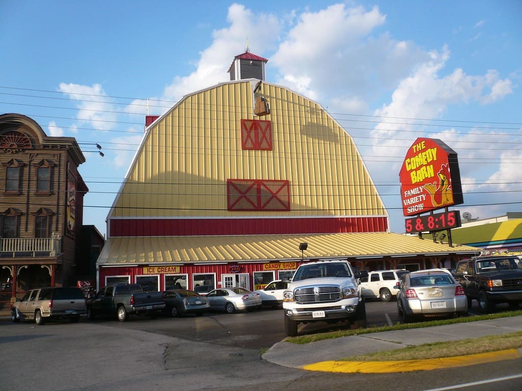 Comedy Barn Theater with a bright red and yellow barn-style exterior in a busy parking lot.
