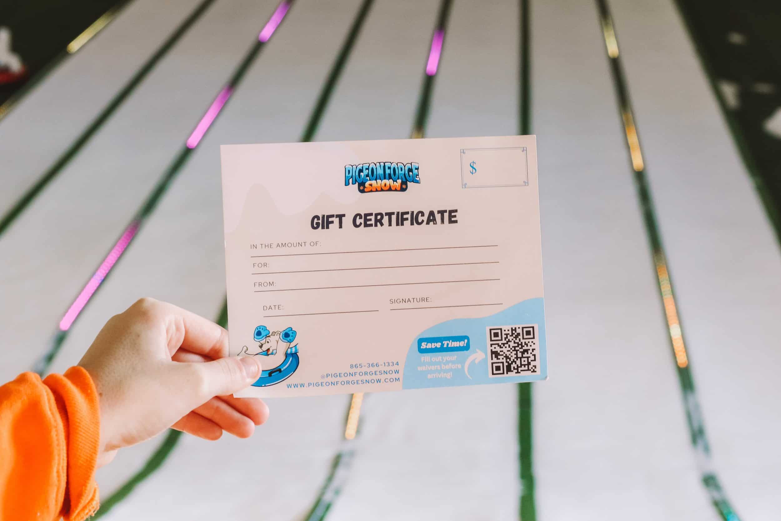 Hand holding a Pigeon Forge Snow gift certificate with indoor snow tubing lanes in the background.