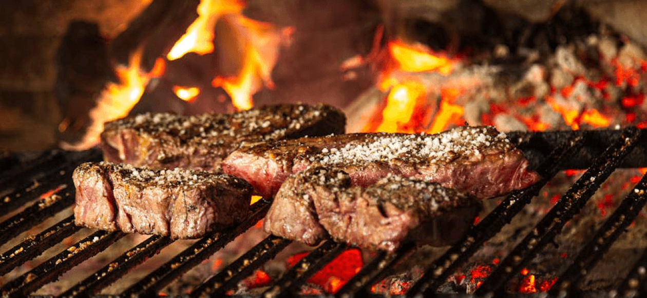 Juicy ribeye sizzling on iron grill over hot coal, a scene visible in most steakhouses in Pigeon Forge.
